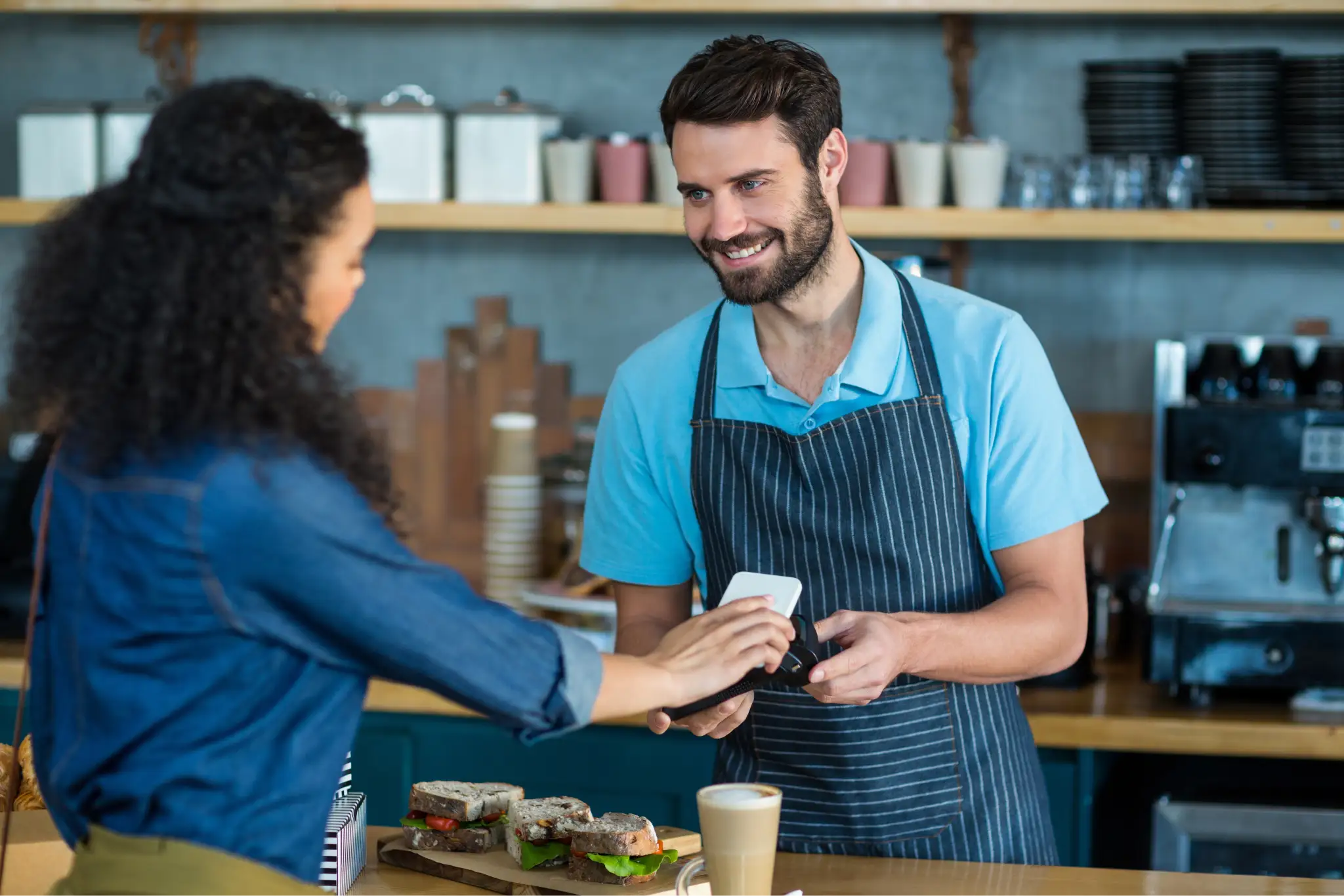 A woman at a deli making a contactless payment by placing her phone on a mobile POS system.