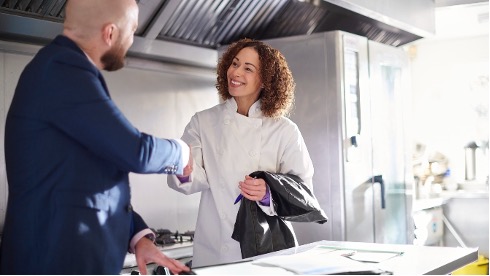 A restaurant owner shakes hands with a merchant services sales rep in her kitchen.