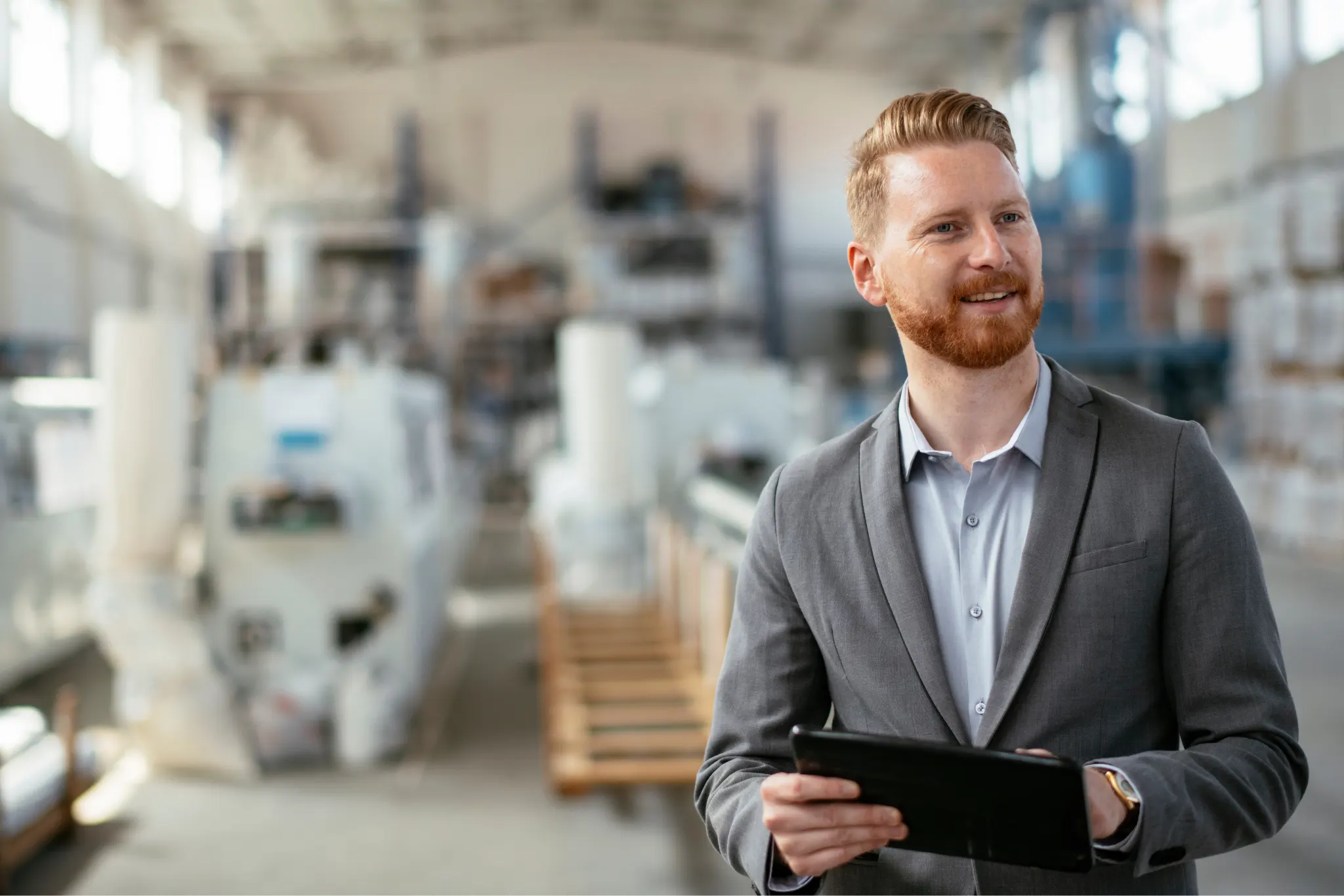 A businessman wearing a suit in a warehouse using a tablet