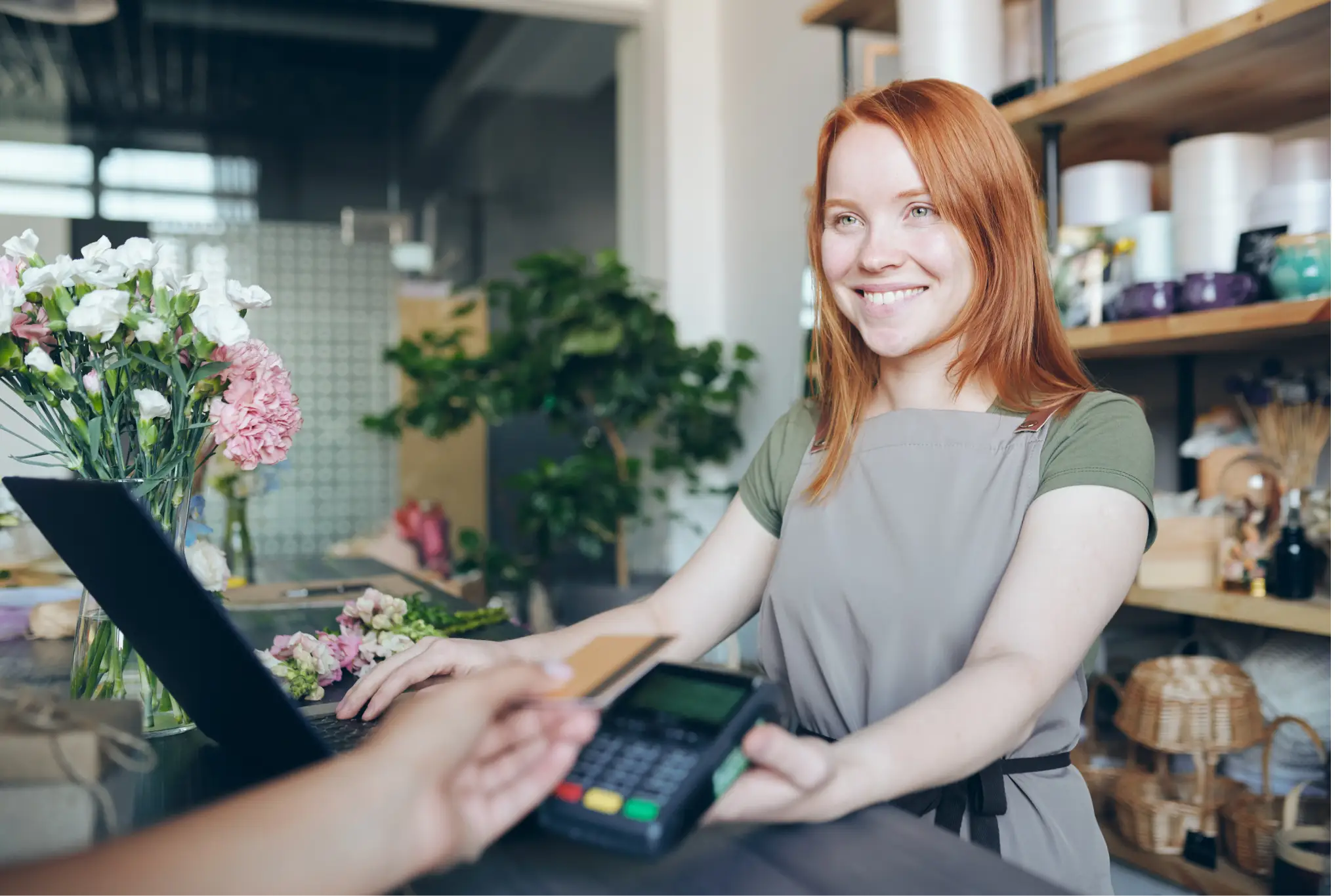 A woman smiling and holding a mobile POS system while someone checks out with a credit card