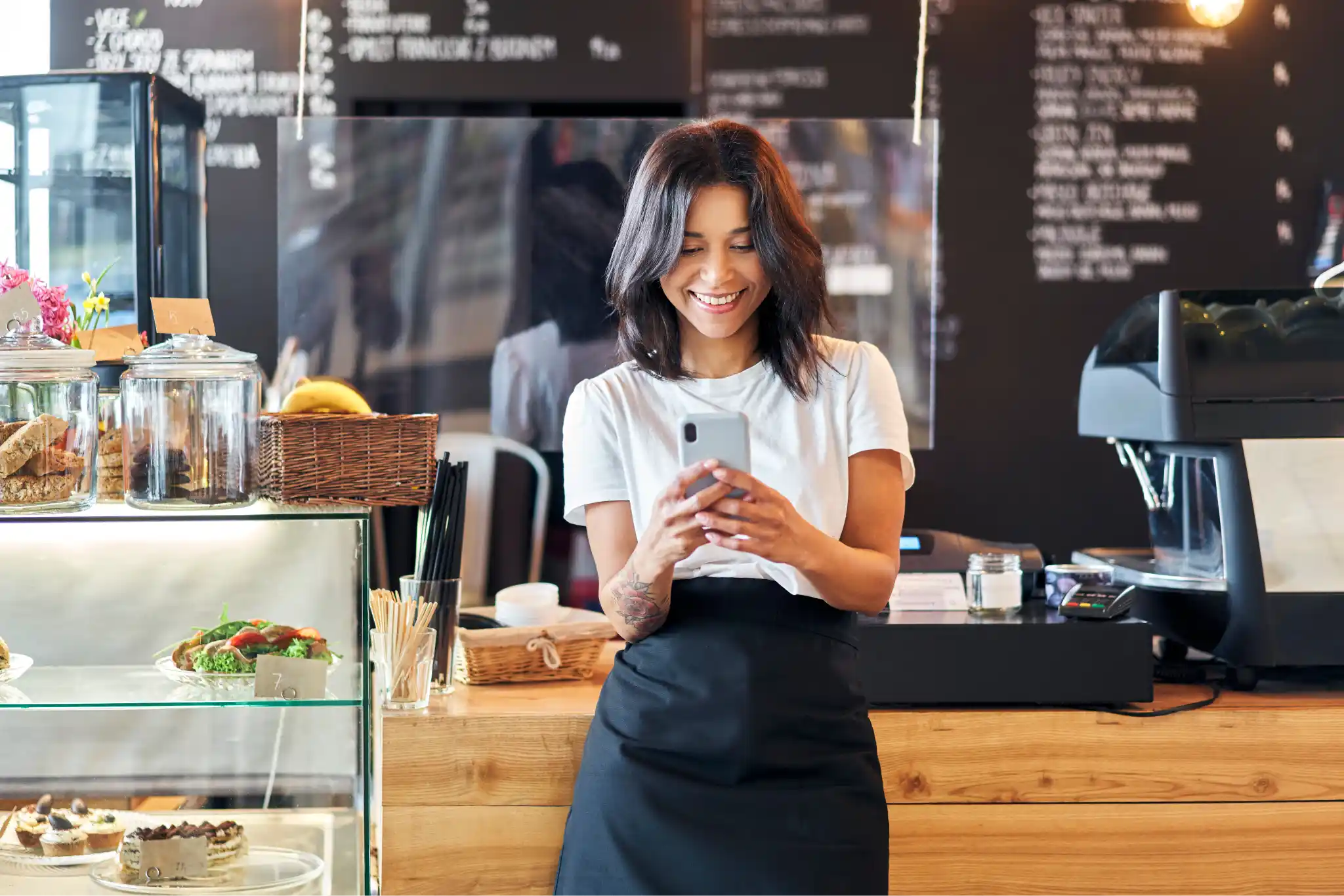 A woman standing in front a café shop counter, using her cell phone